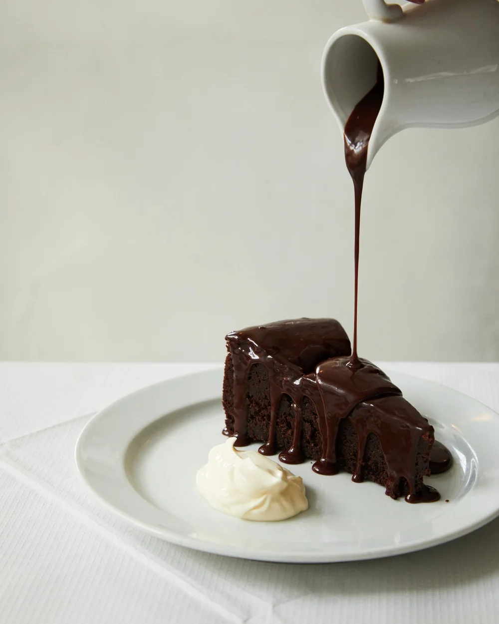 chocolate brownie on white plate and tablecloth with chocolate sauce by st john