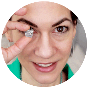Close-up of a woman smiling, holding a diamond near her face.
