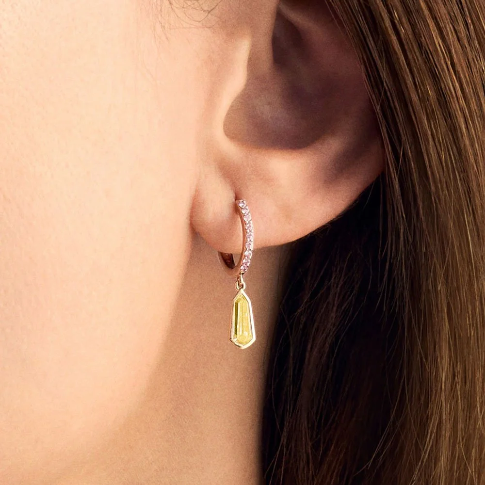 Close up of yellow and pink diamond huggie hoop earrings on woman's ear