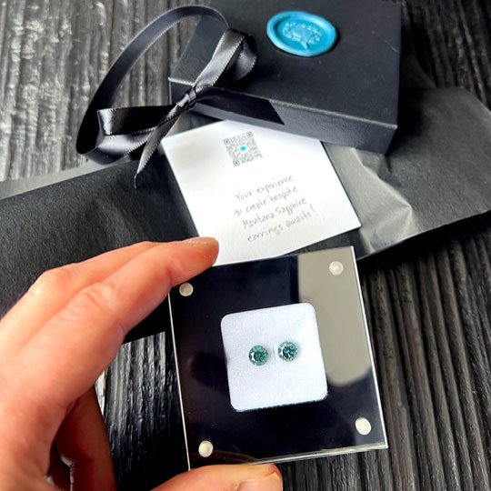 A personalized bespoke jewelry gift box opened up to reveal two sapphires for stud earrings