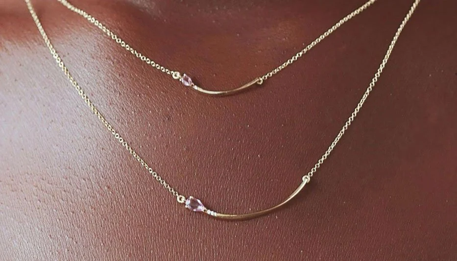 two pink sapphire and gold layering necklaces worn on a woman's neck