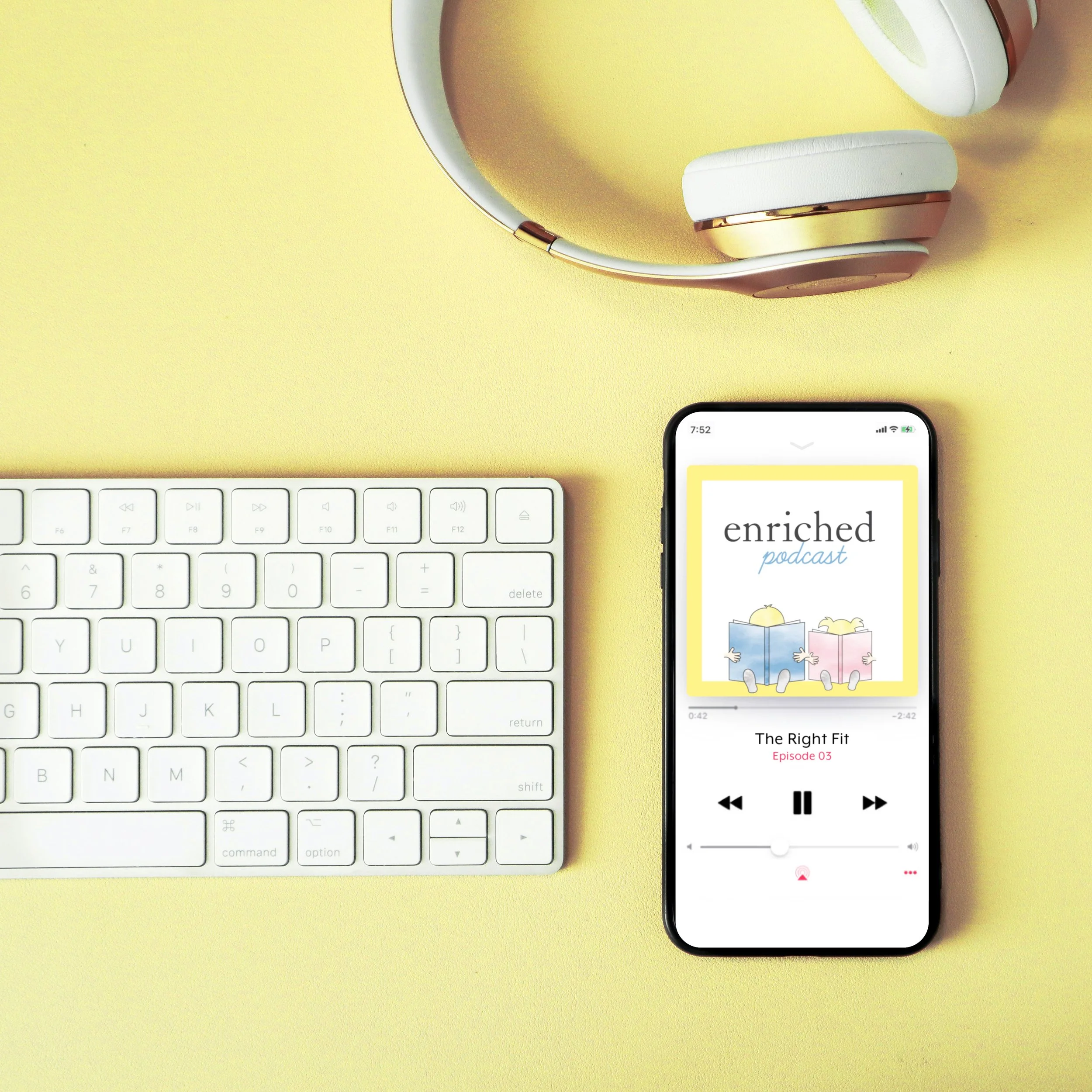 An iPhone displaying the Enriched Podcast beside a keyboard and headphones.