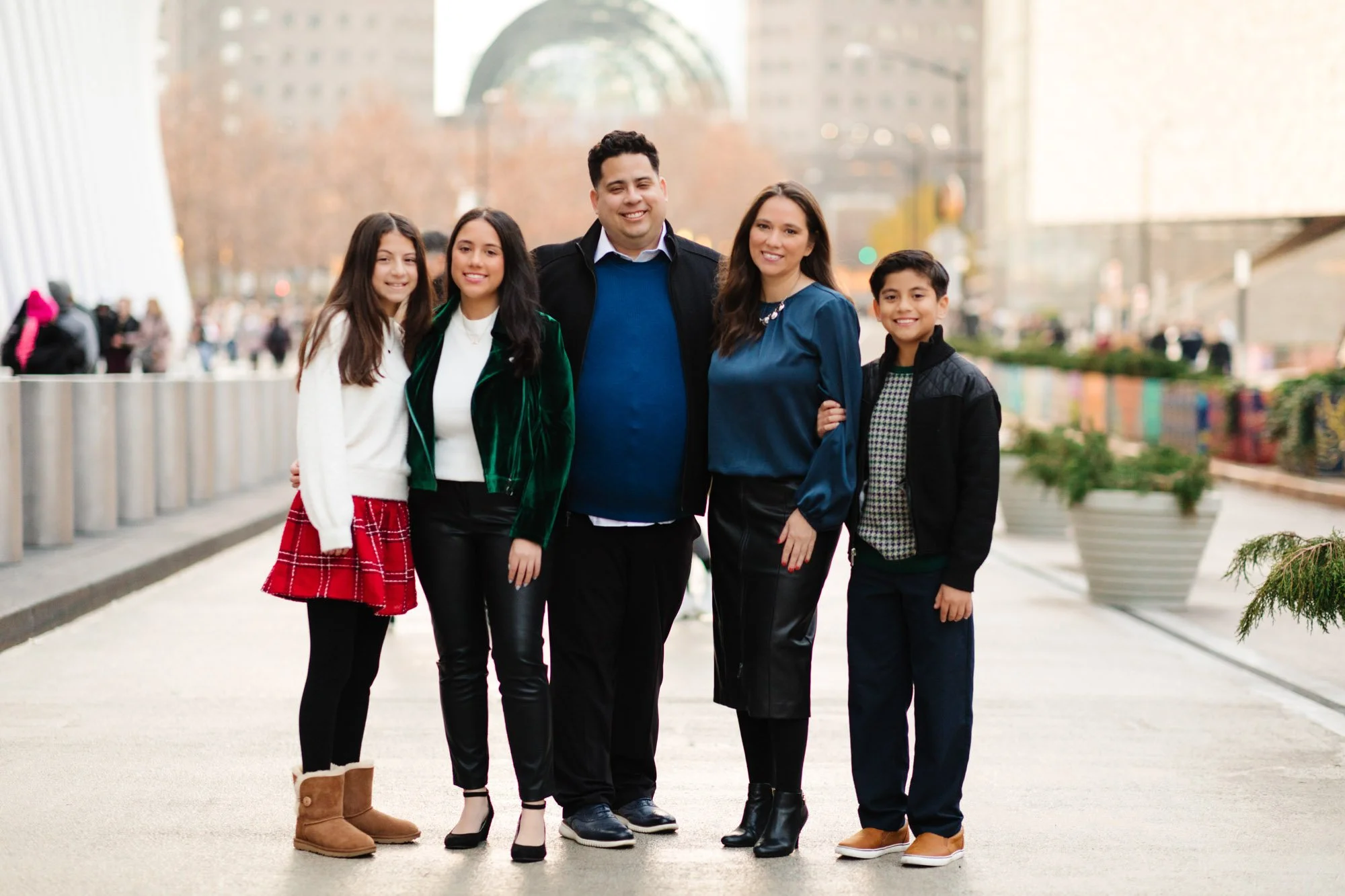 Family of five posing outdoors in a city setting with modern architecture in the background.