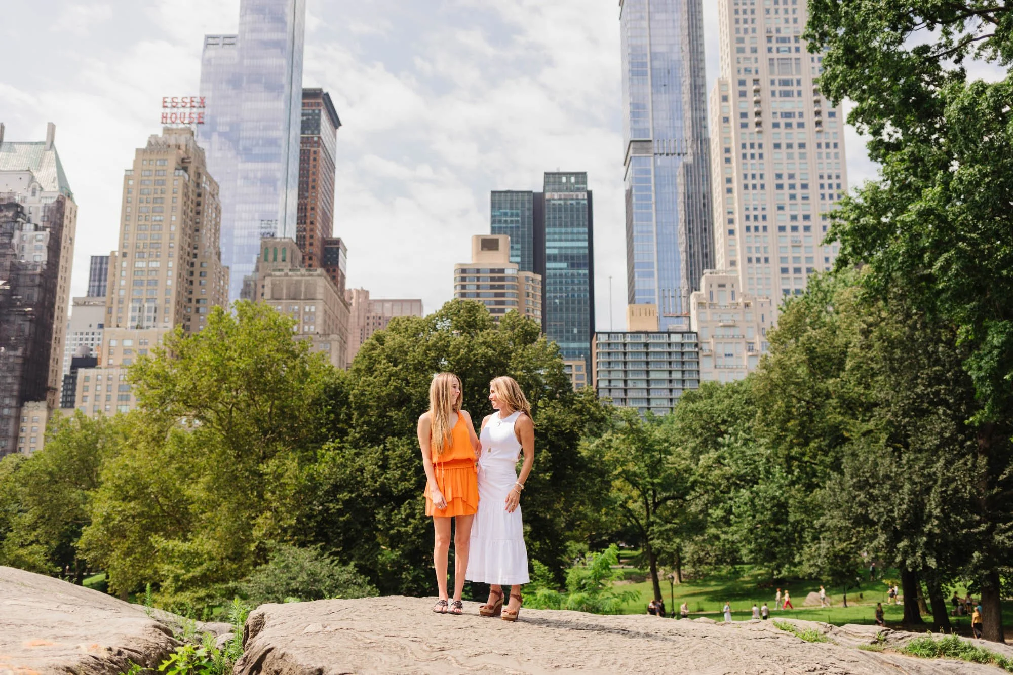 Two women standing on a rock in Central Park with city skyscrapers in the background.
