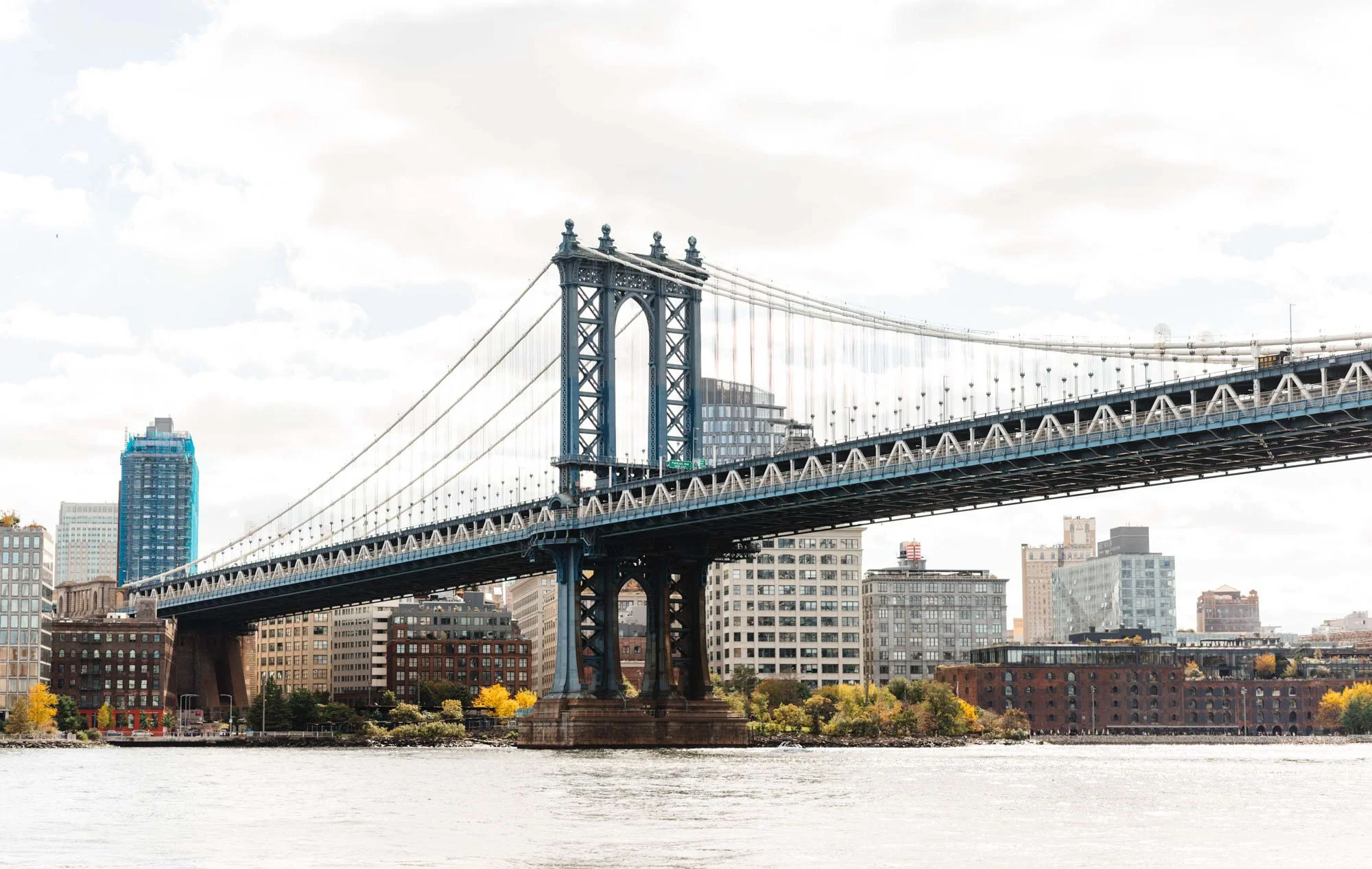 Manhattan Bridge spanning across a cityscape with buildings and river.