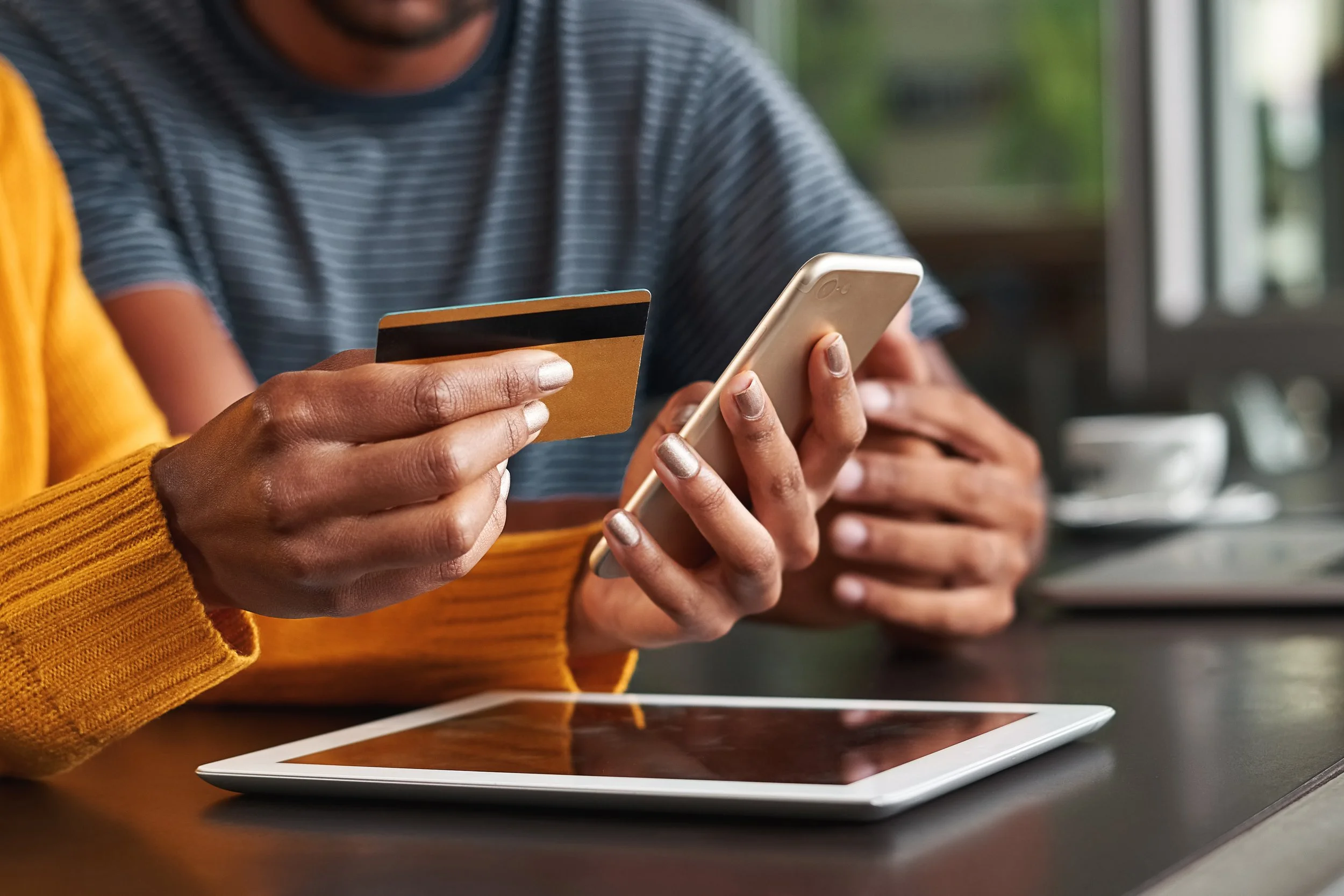 Image of woman making a credit card payment using her phone. A man sits next to her in the background of the shot.