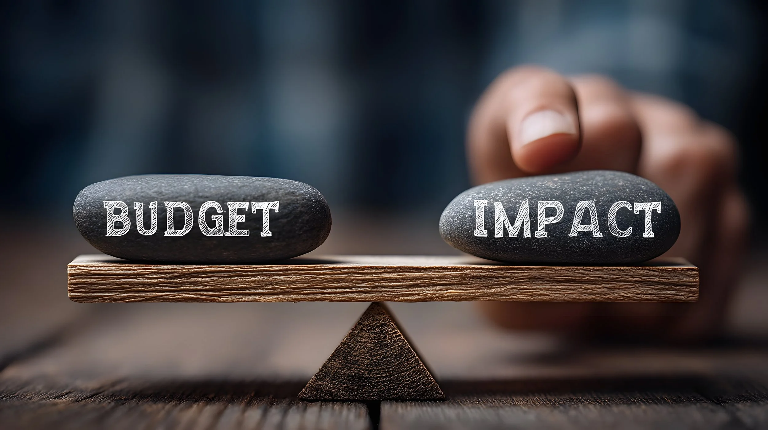 An image of two rocks balancing on scales.  Each rock has a word written on it - "Budget" and "Impact"