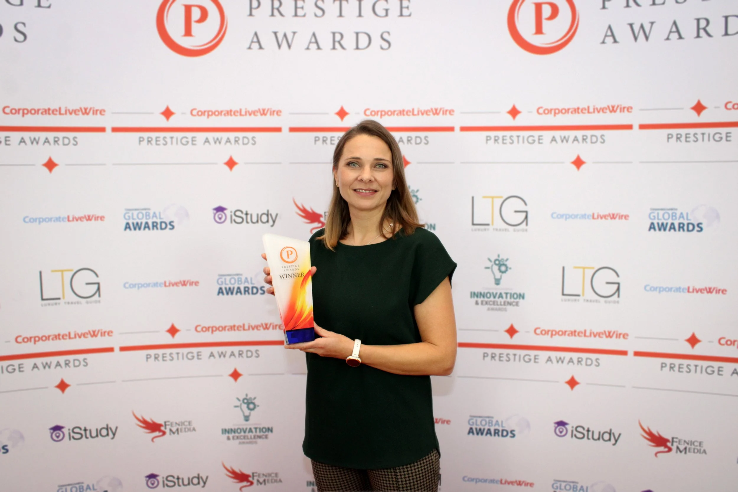 Tyra Oseng-Rees holding an award trophy with a backdrop displaying various sponsor logos and 'Prestige Awards' text.