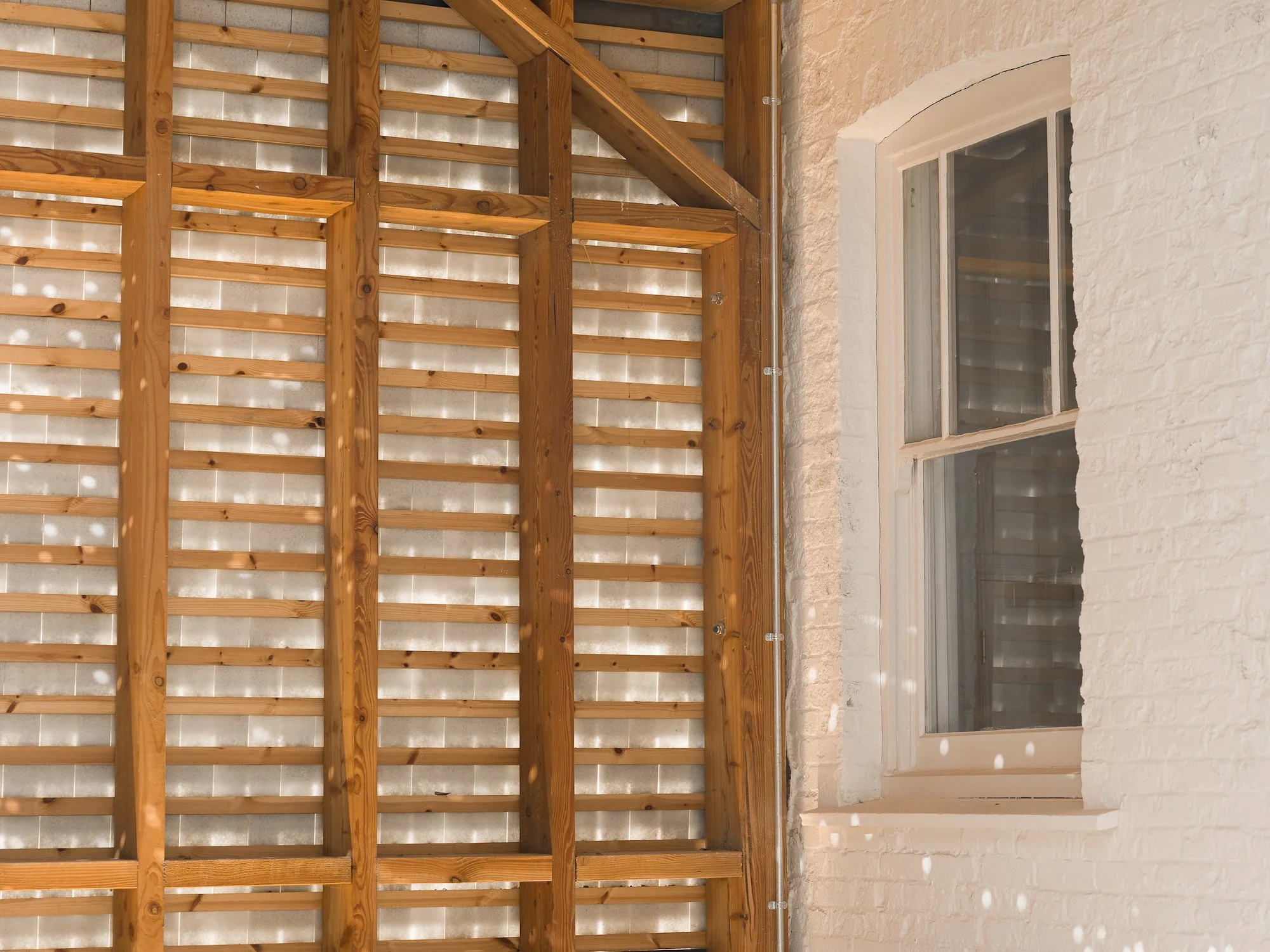 Close up view of the interior recycled glass at the Buttermarket, showing a window framed by wooden structures supporting the glass tiles and slate. The image highlights the light penetration through the glass tiles. Photo: Claire Fear
