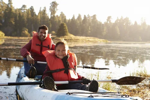 Man and child rowing through a river on a kayak