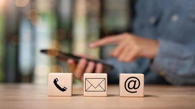 Three wooden blocks demonstrating the signs of a phone and email to demonstrate the ability to contact