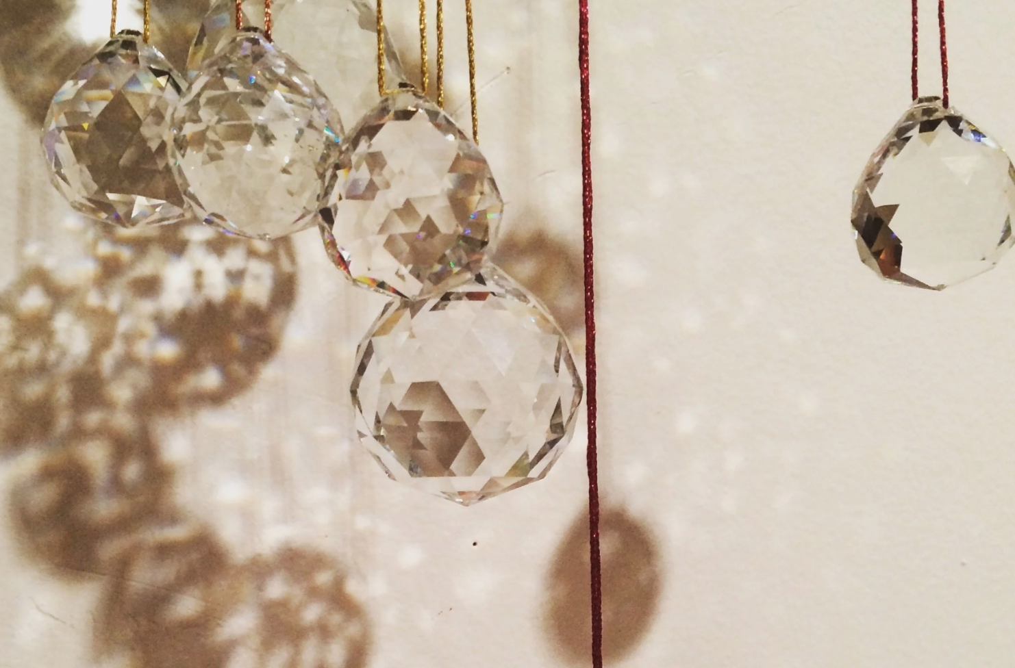 Close-up of hanging glass or crystal ornaments with red and gold strings, casting shadows on a white surface.
