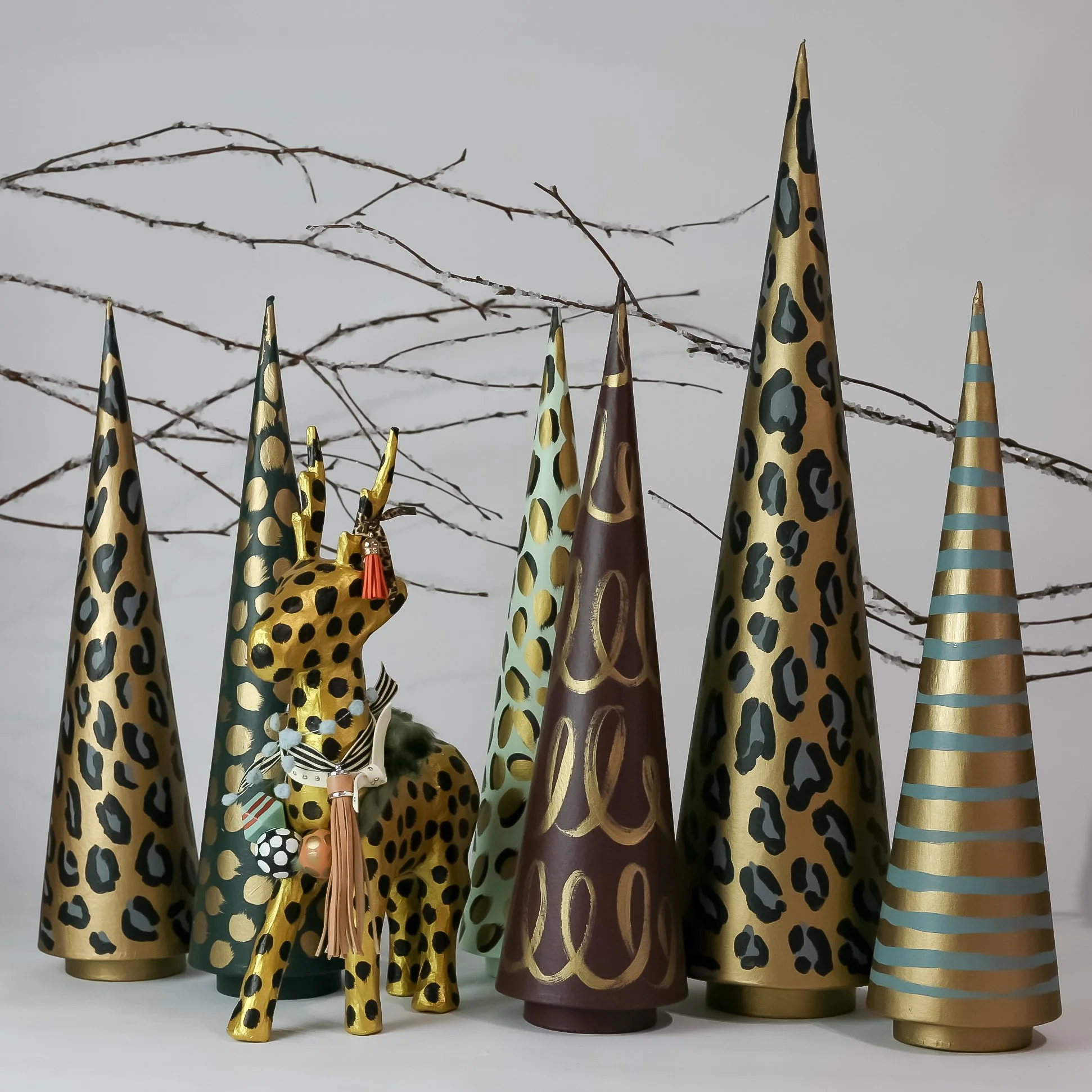 Collection of decorative cone-shaped objects with animal print patterns, including a purple and gold giraffe figurine with accessories, and thin bare branches in the background.