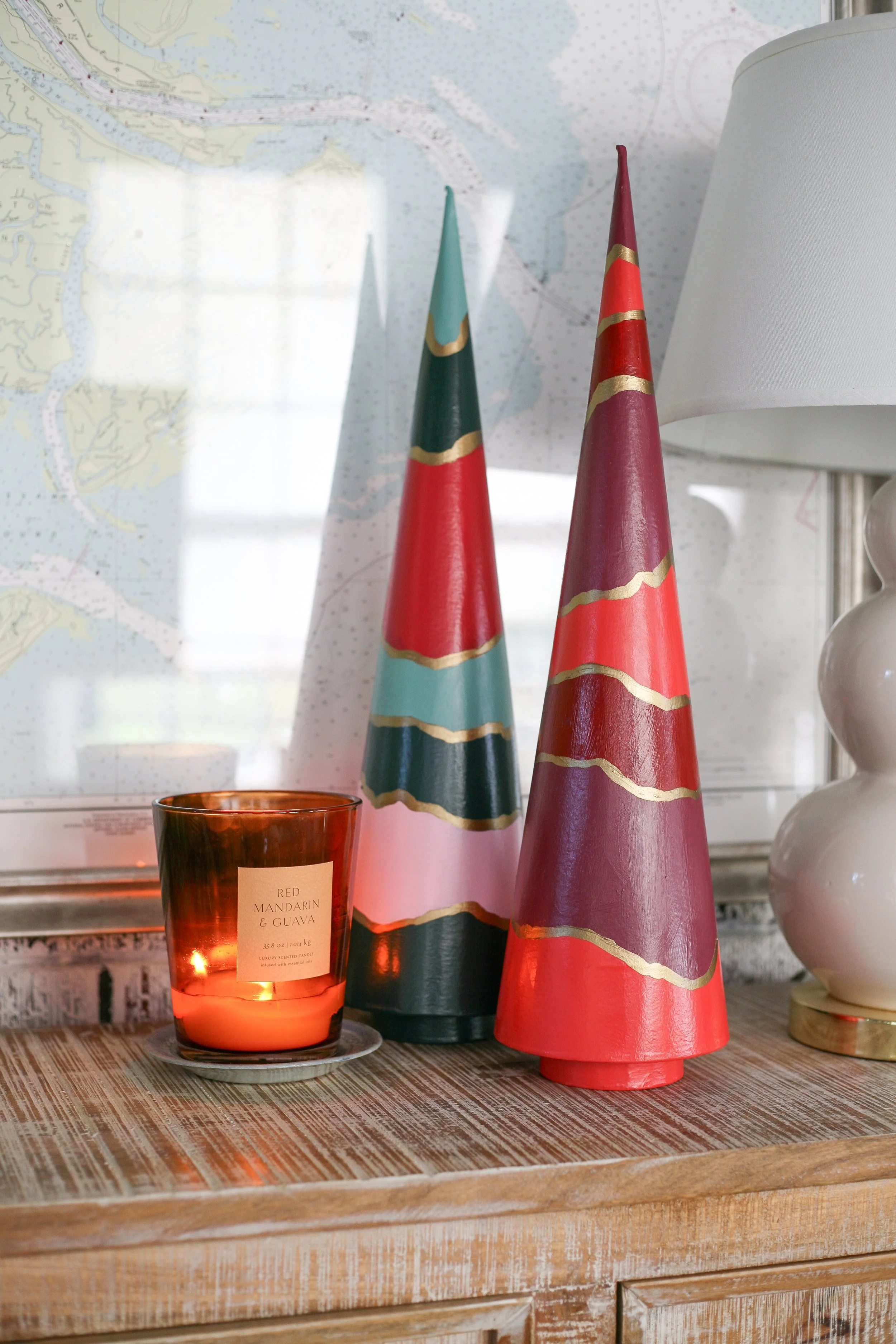 Decorative Christmas trees, a candle, and a lamp on a wooden surface with a nautical map in the background.