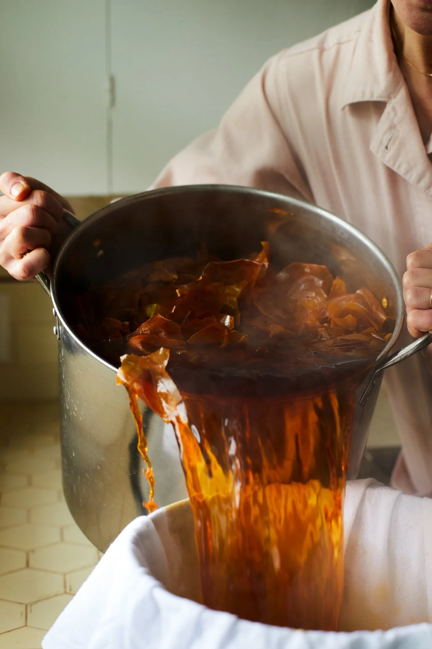 Person pouring liquid with onion skins from a pot into a cloth-lined bowl.