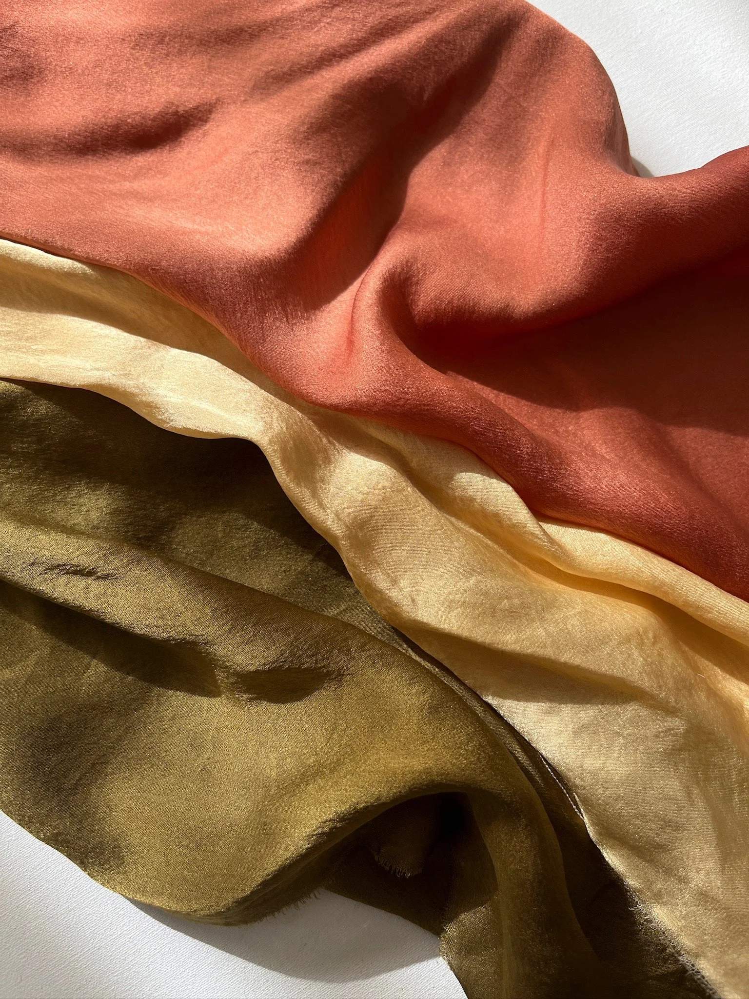 Close-up of three overlapping pieces of fabric in shades of orange, beige, and olive green.