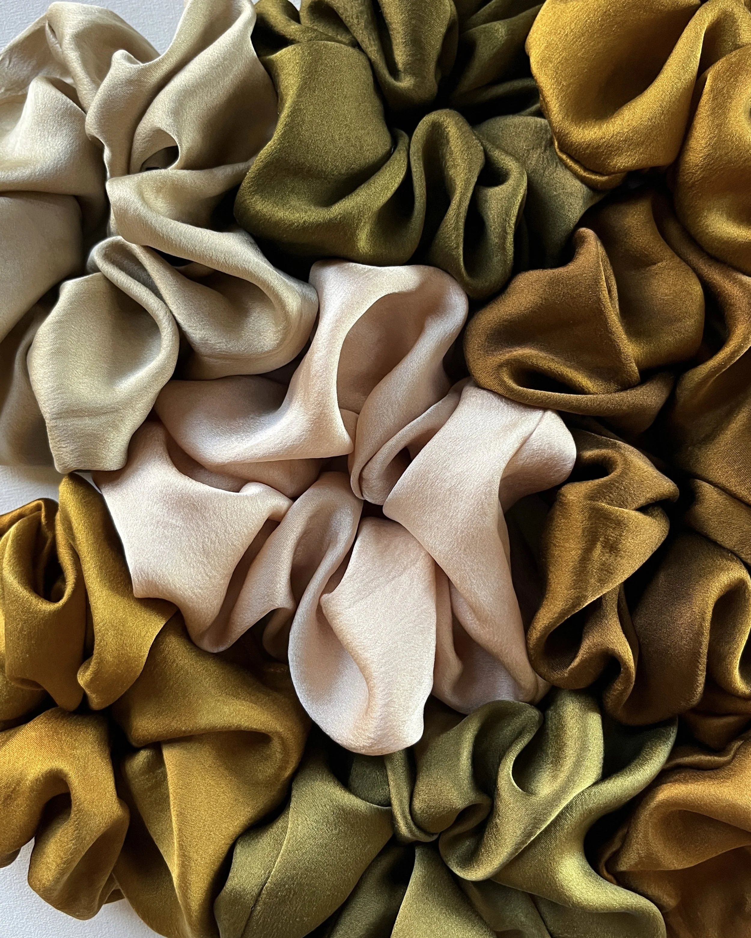 Close-up of several silk scrunchies in beige, olive, and gold colors.
