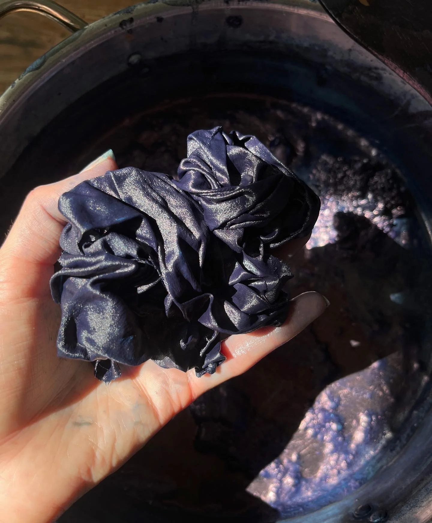 Hand holding crumpled, dyed fabric above indigo dye vat