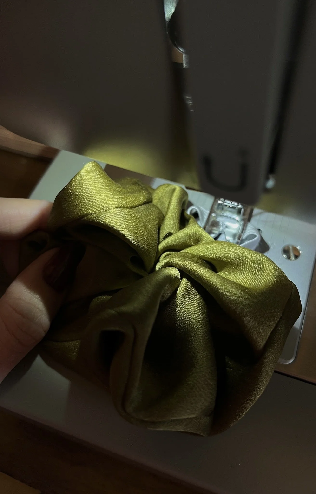 Person sewing green satin fabric on a sewing machine