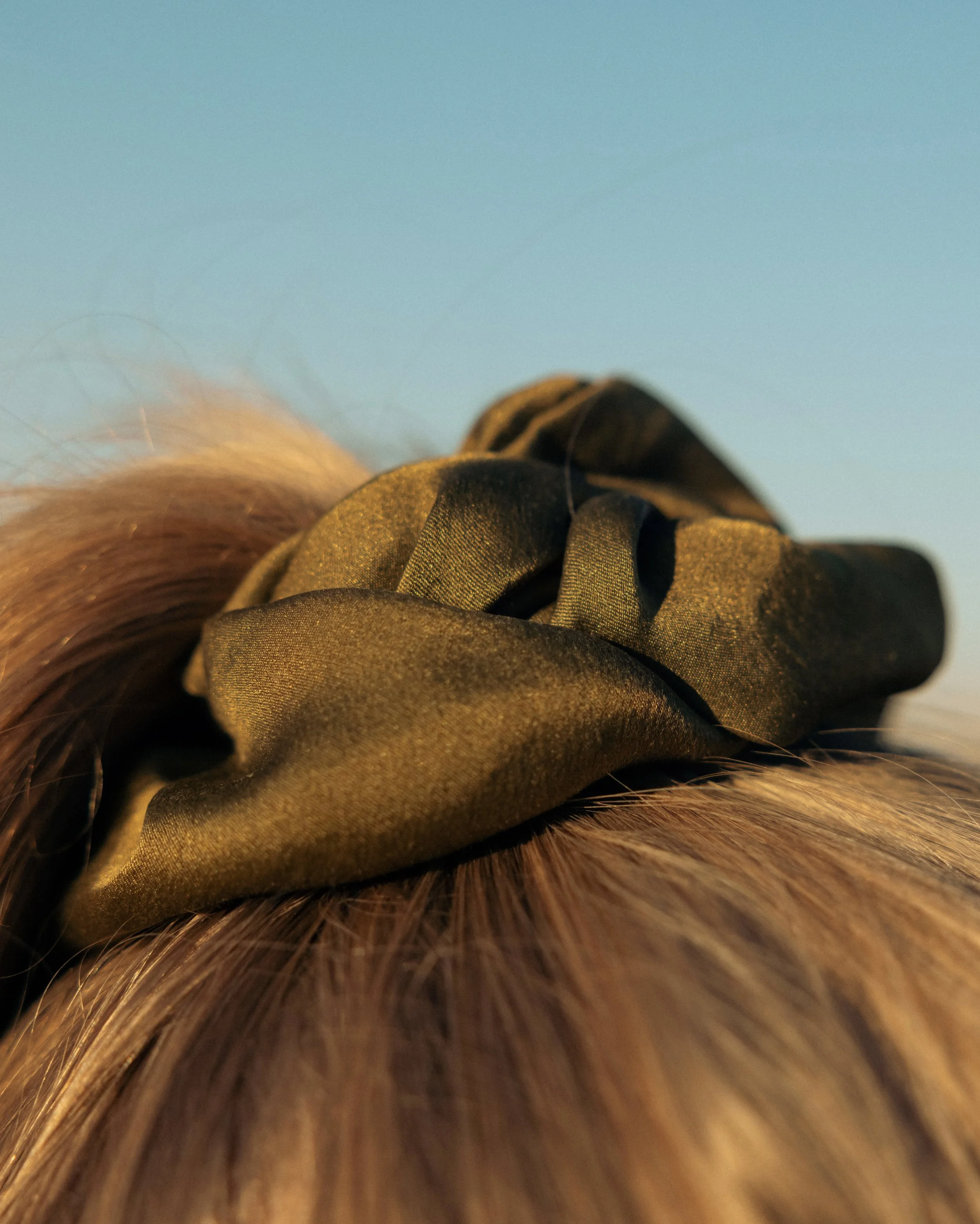 Close-up of a brown hair bun with a green velvet scrunchie against a clear blue sky.