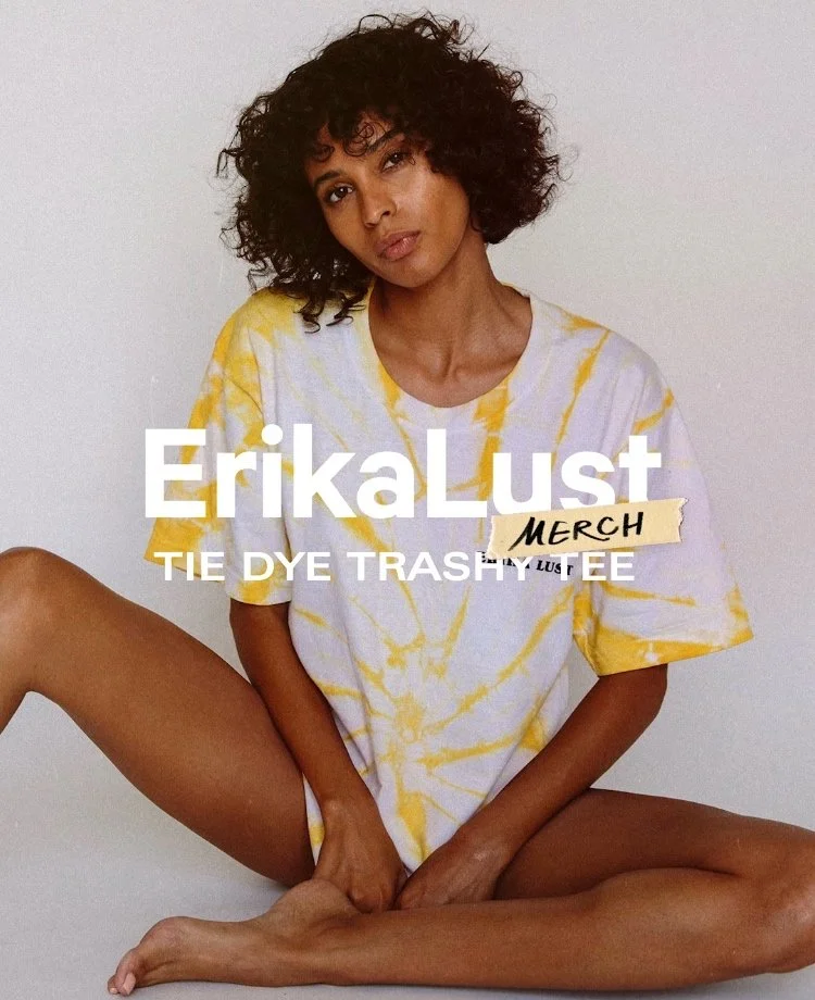 Model wearing yellow tie-dye T-shirt, sitting with legs crossed, promoting Erika Lust merch.