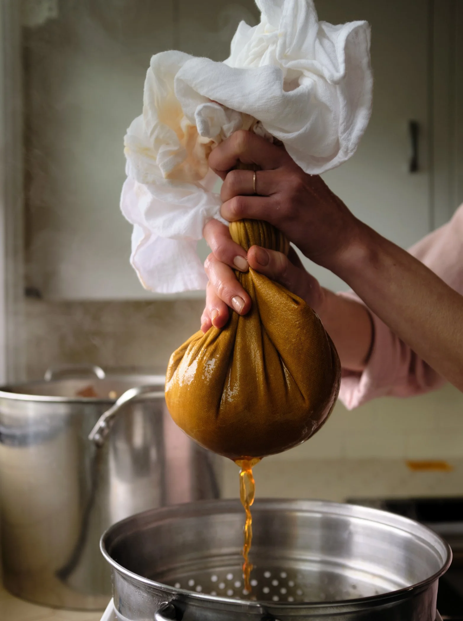 Person squeezing natural dye from a cloth bundle over a pot in a kitchen setting.