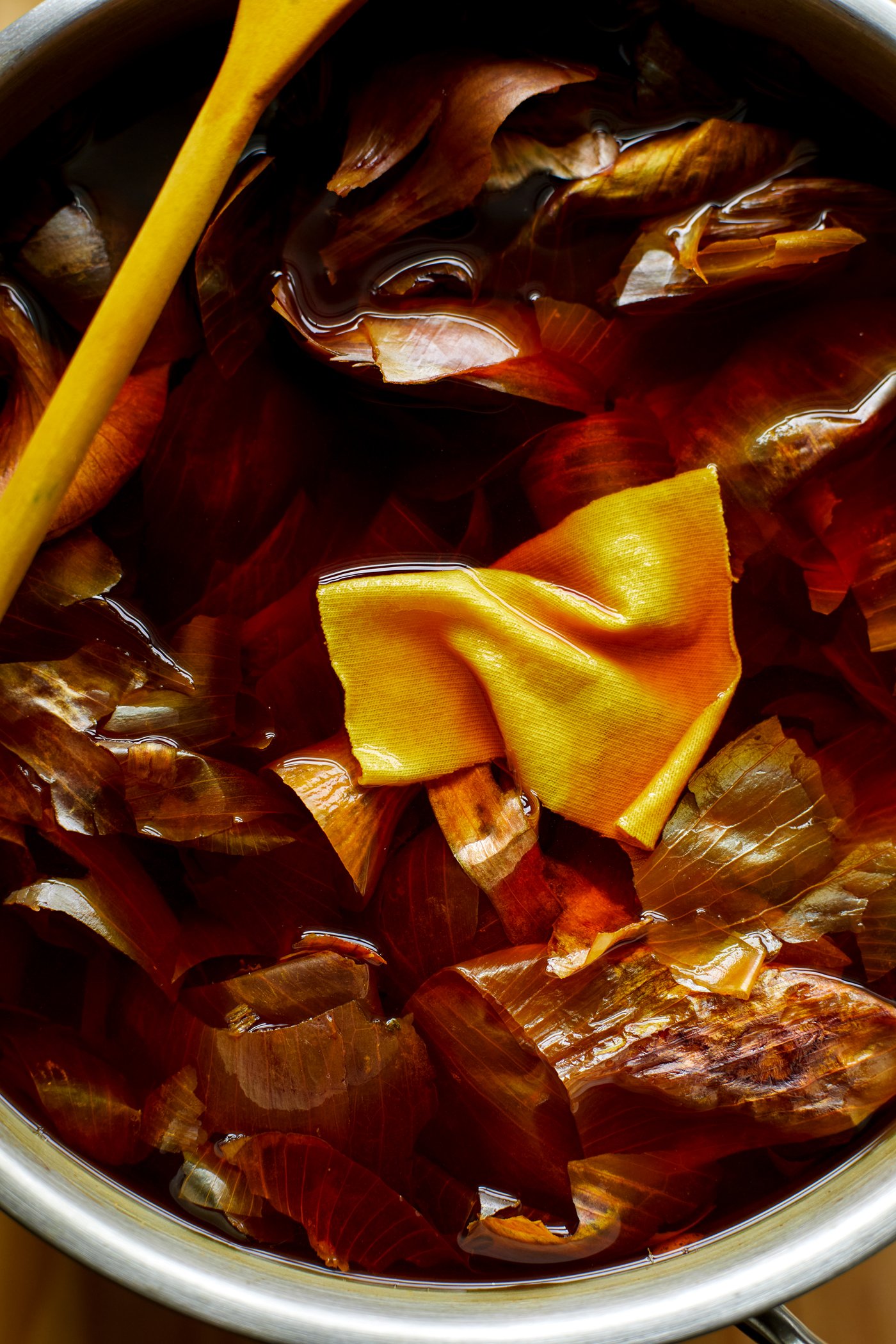 Onion skins and a yellow fabric piece in water for natural dyeing in a pot.