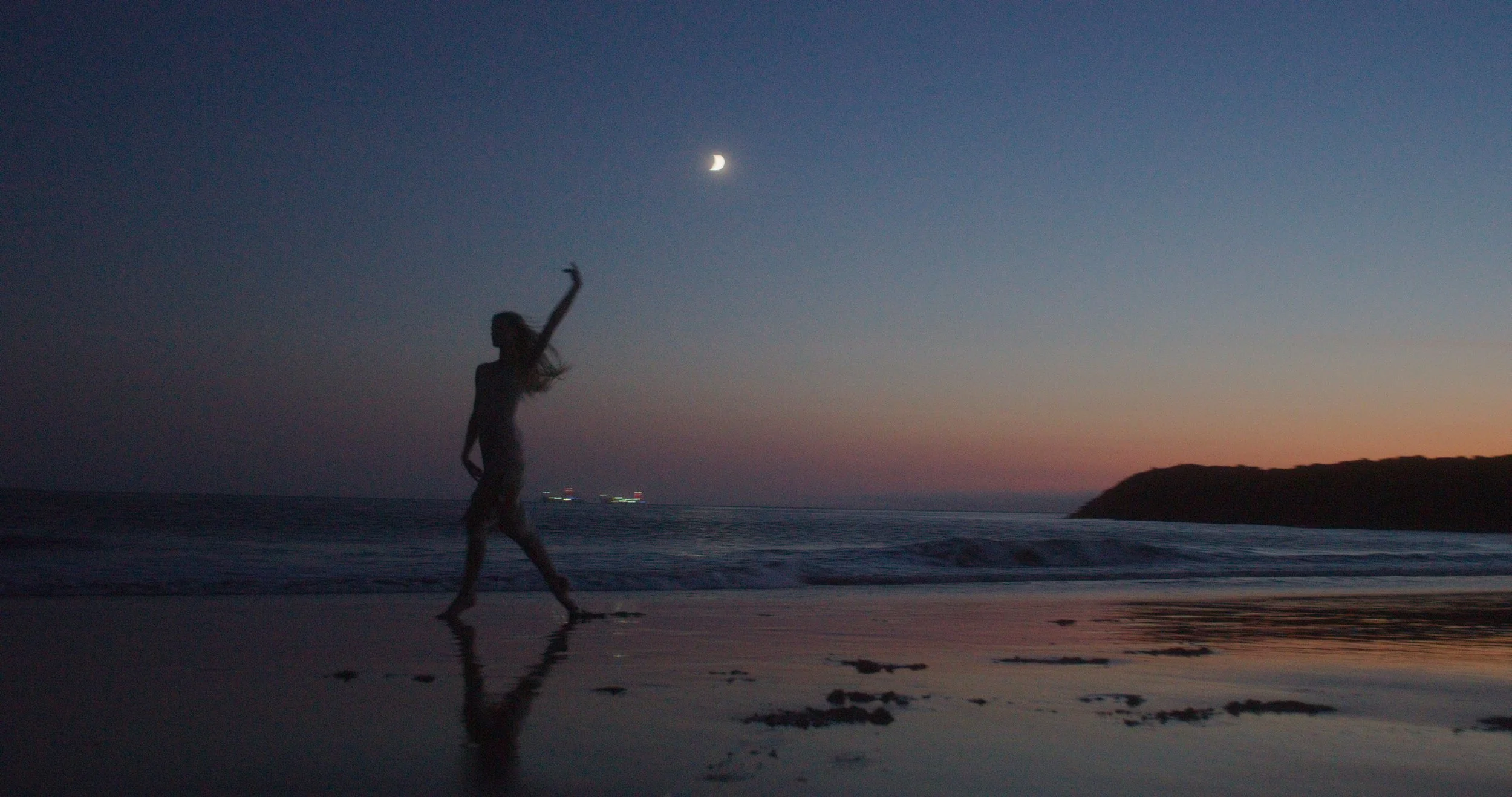 Silhouette of a person dancing on a beach at dusk with a crescent moon in the sky.