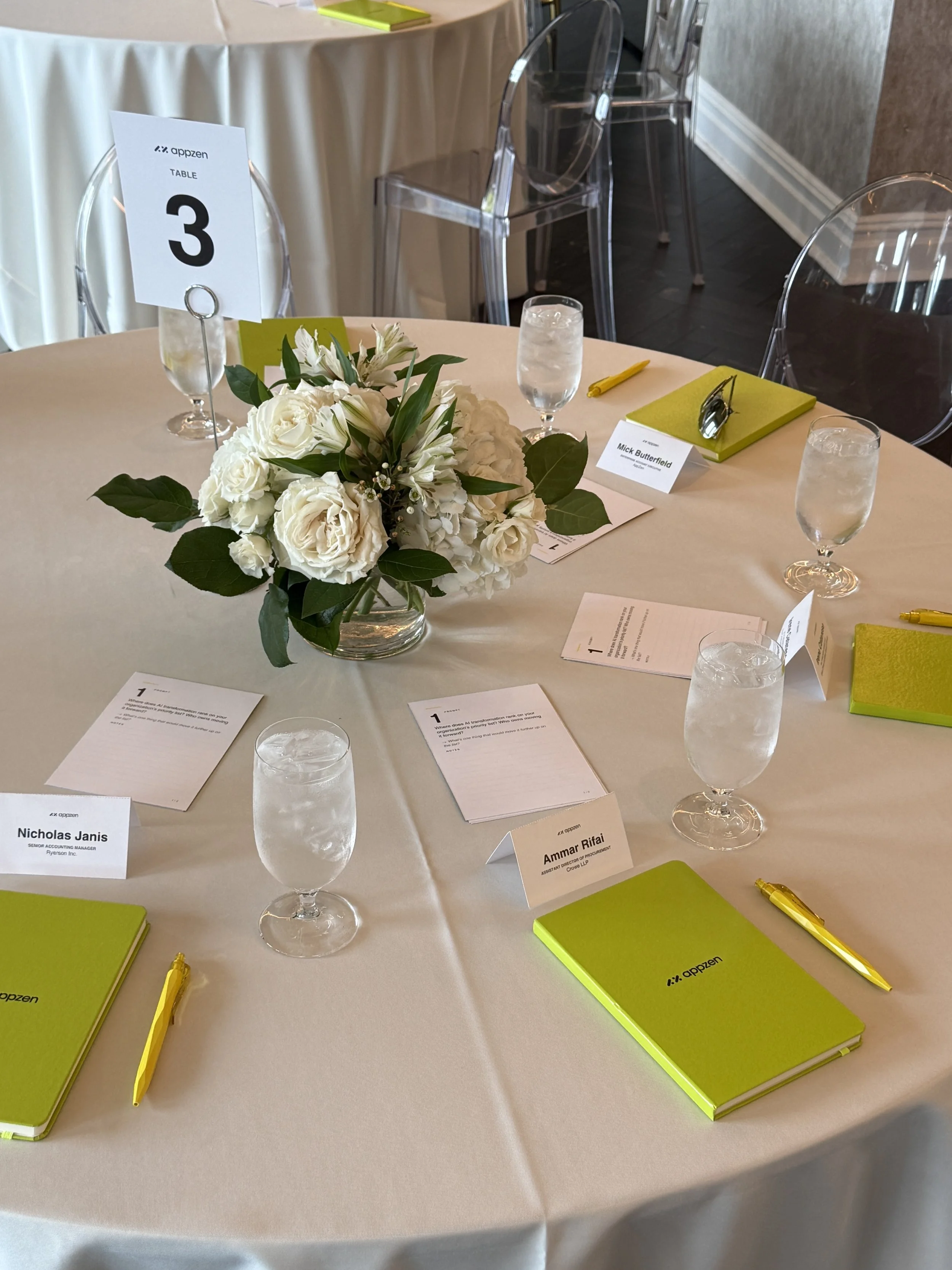 A round table set for a meeting with a floral centerpiece, three glasses of water, green notebooks, yellow pens, and name cards. LM Studio Chicago private dining corporate events.