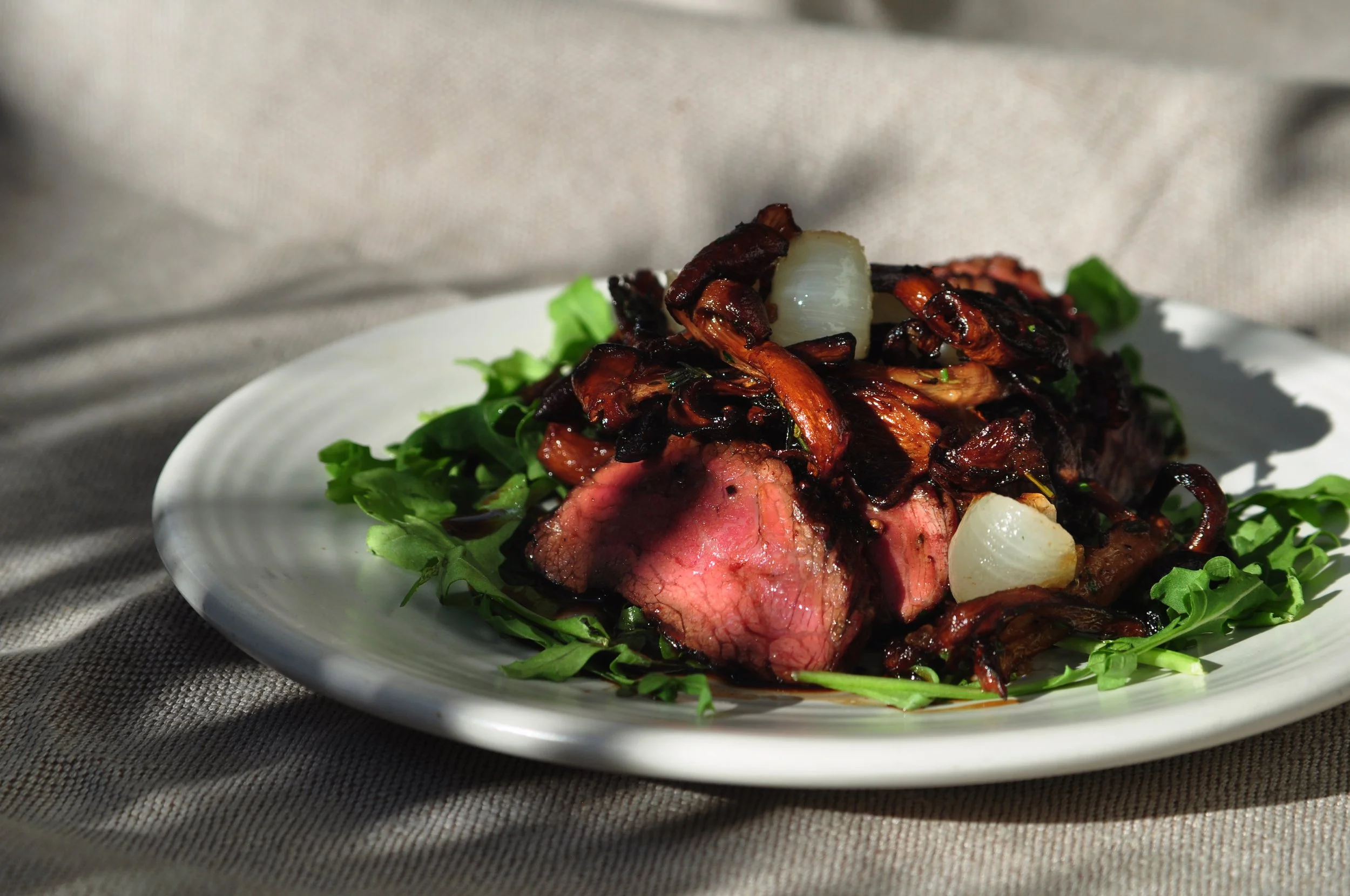 hanger steak, chanterelles, cipollini onions & arugula  on a white plate