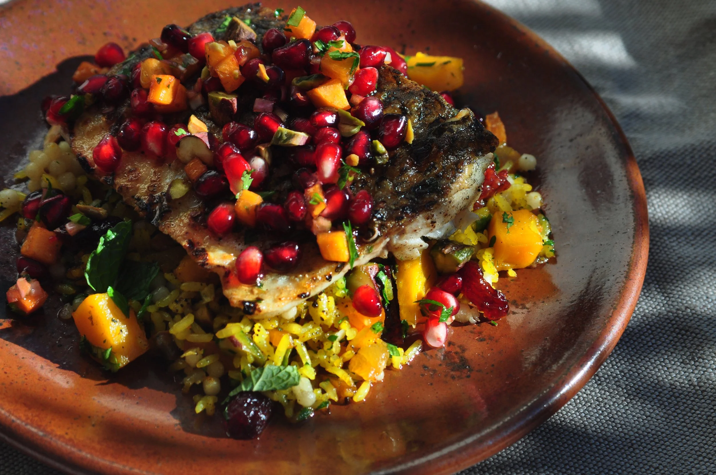 grilled sea bass, jeweled rice, persimmon-pomegranate salsa & pistachios on an orange plate