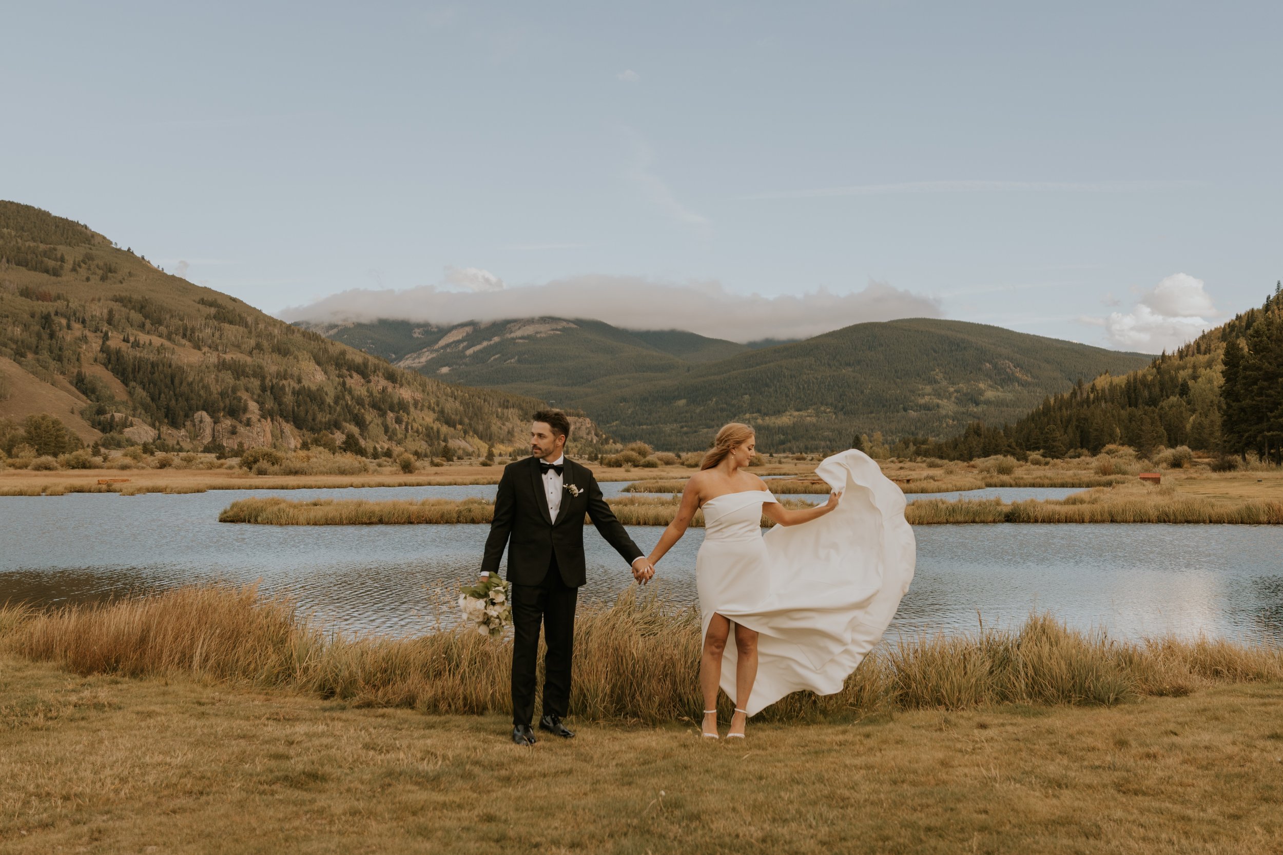 bride and groom standing next to a lake at Emmy & Dick's Chic, Sophisticated Black-Tie Vail Wedding