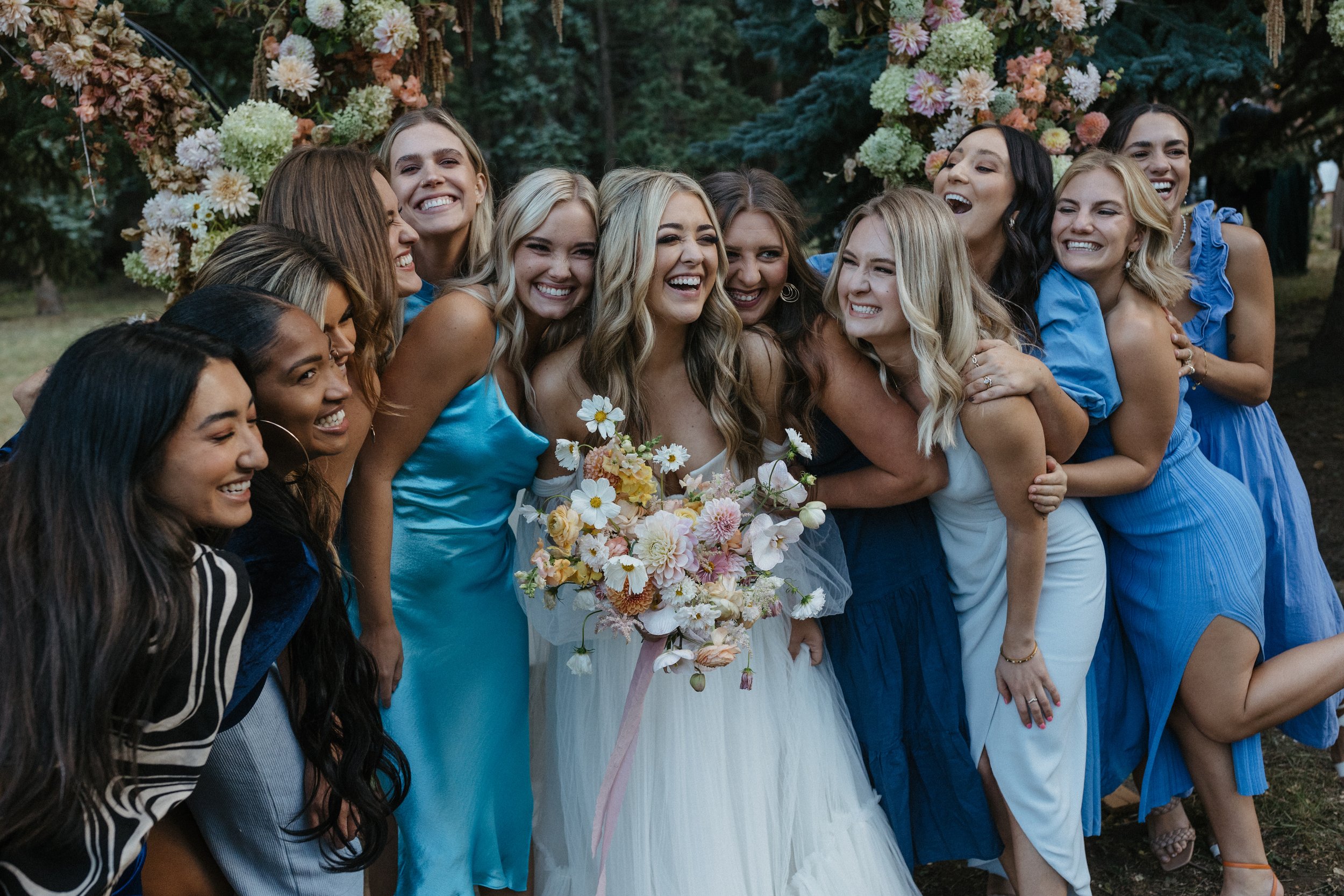 bride and her bridesmaids standing in front of a ceremony arch at a wedding with a colorful wedding palette