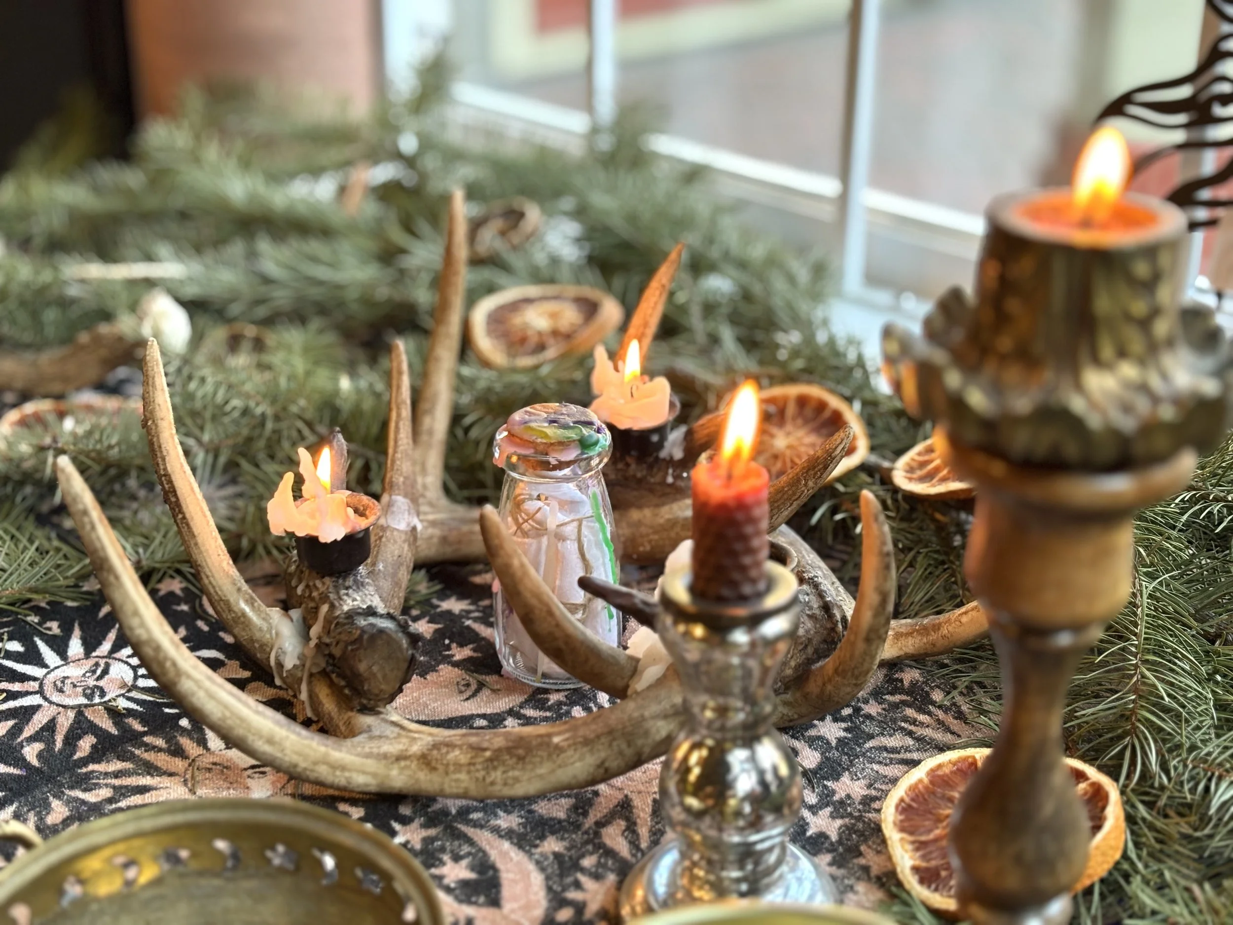 A festive altar with candles, dried orange slices, and pine greenery, featuring antlers as a base for the decor.