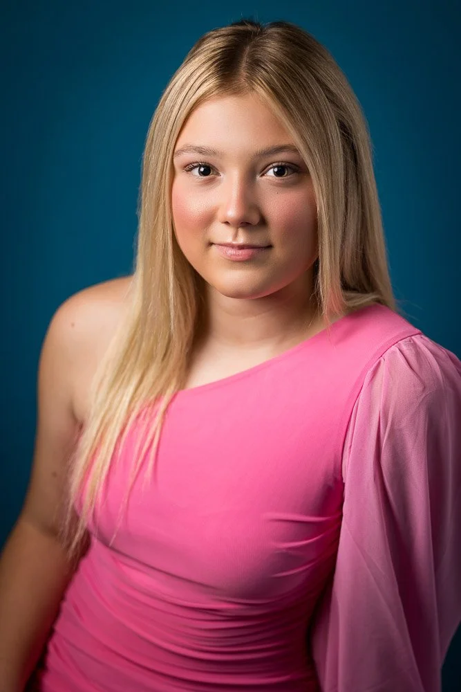 blonde girl in pink dress in front of a blue wall looking up at the camera