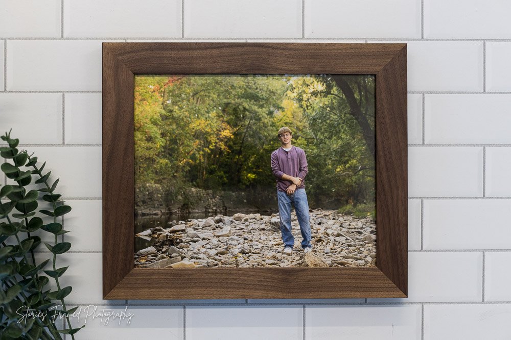 Tosa West Class of 2026 senior Calvin in a walnut framed wall print by a river, Waukesha senior portraits