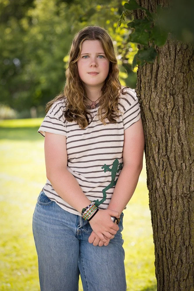 high school senior girl in striped shirt leaning on a tree