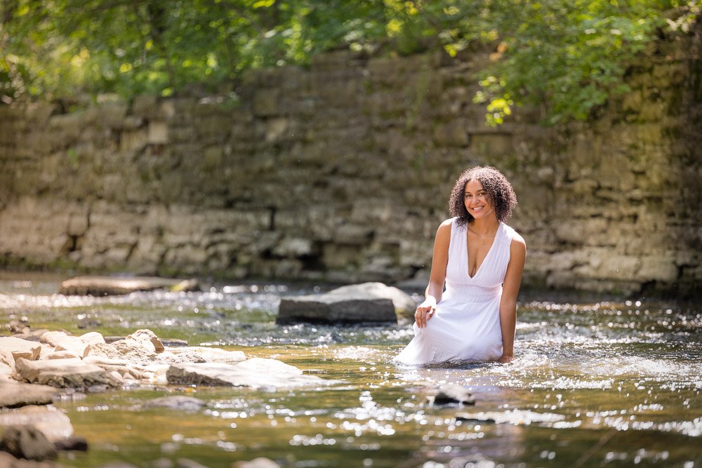 senior girl in a white dress perched on a river rock