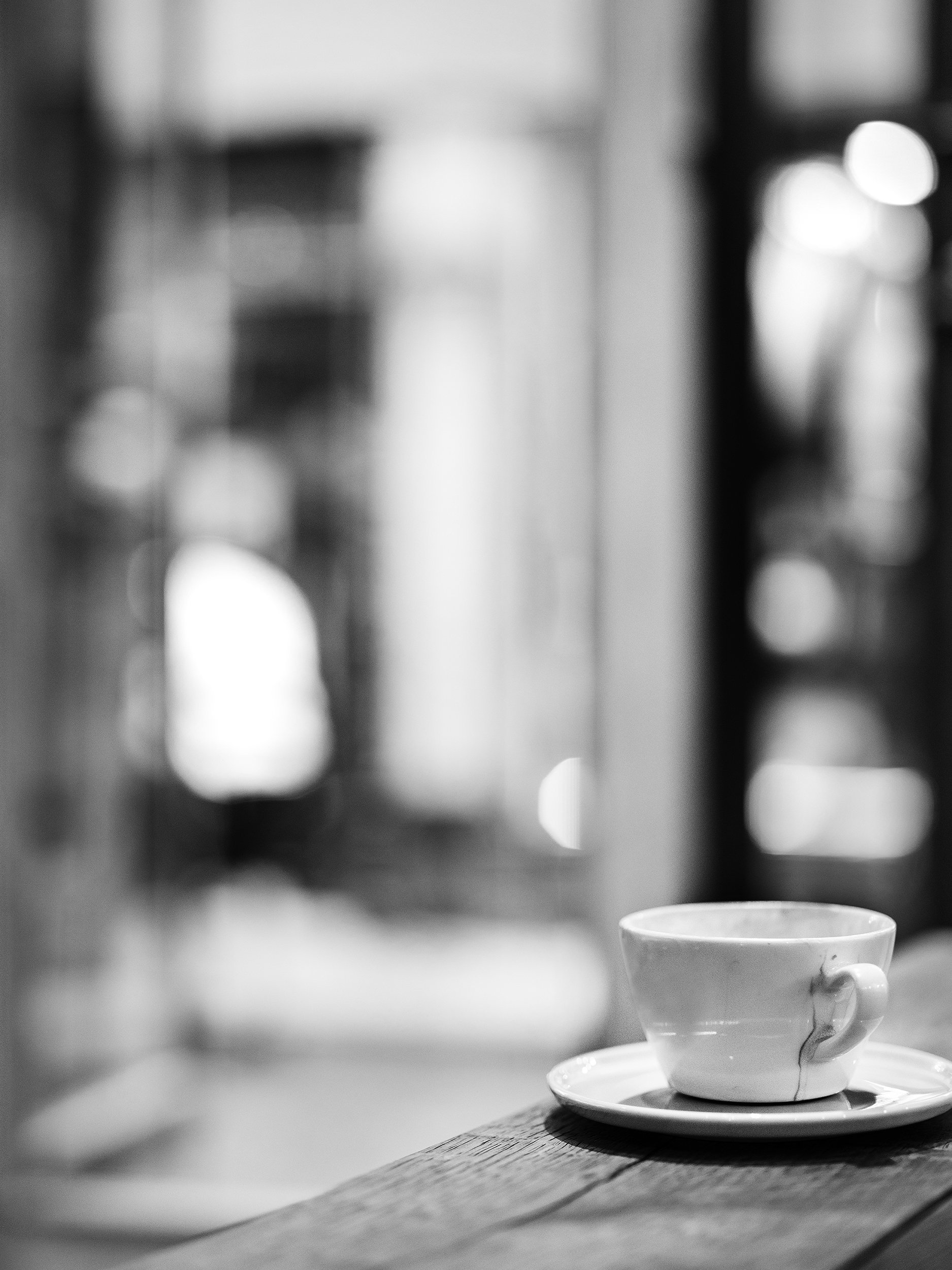Black and white photo of a coffee cup on a wooden table with blurred background.