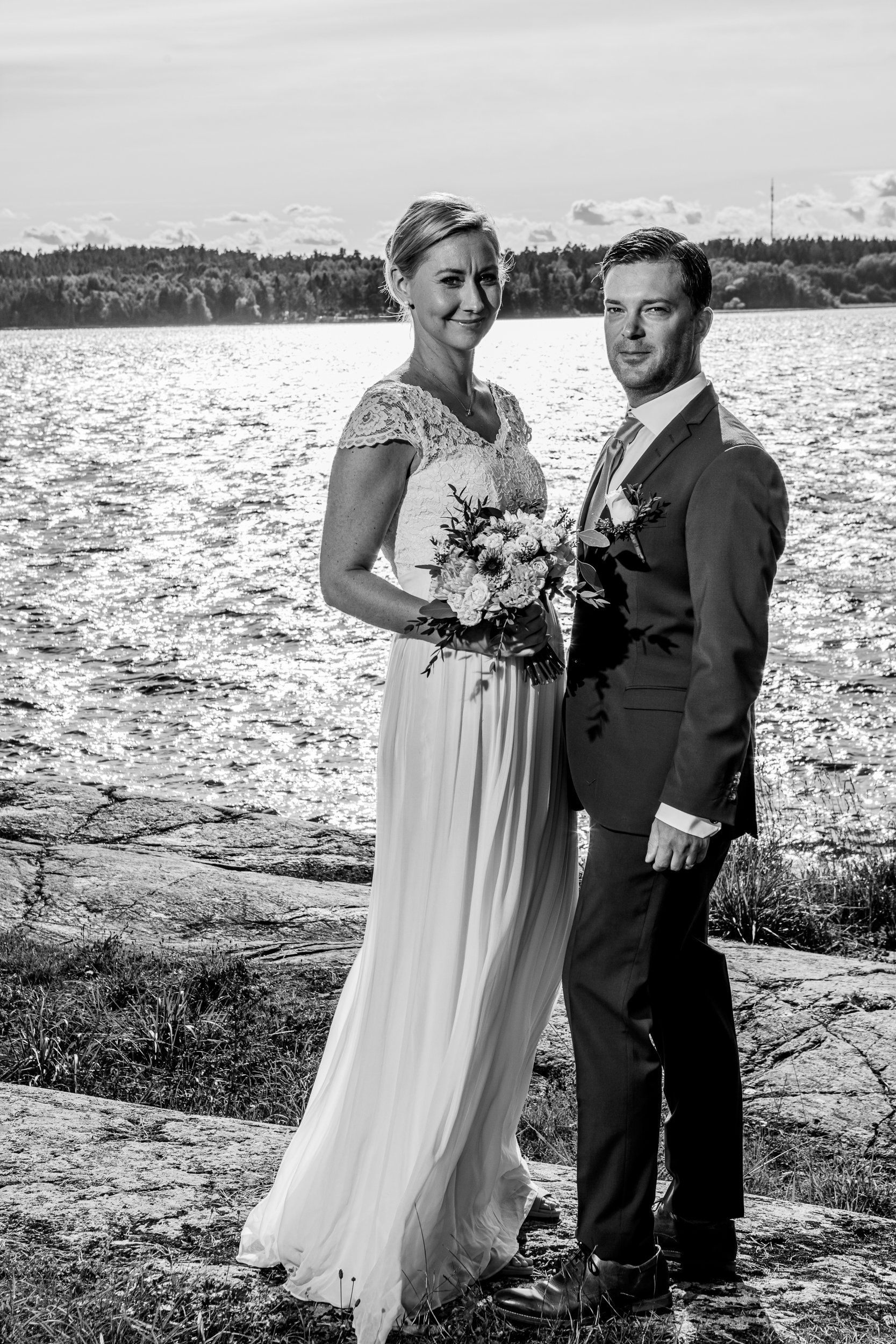 Black and white photo of a bride and groom standing by water.