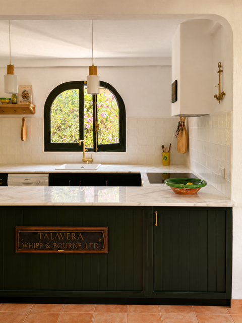 Cocina con ventana arqueada, lavavajillas, fregadero con grifo dorado, utensilios de cocina y tazones en la encimera, decoración en tonos neutros con detalles en dorado.