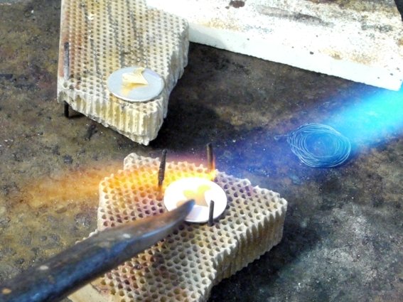 Mit der Flamme erhitzt wird das Feingold mit einem Stahl angerieben.