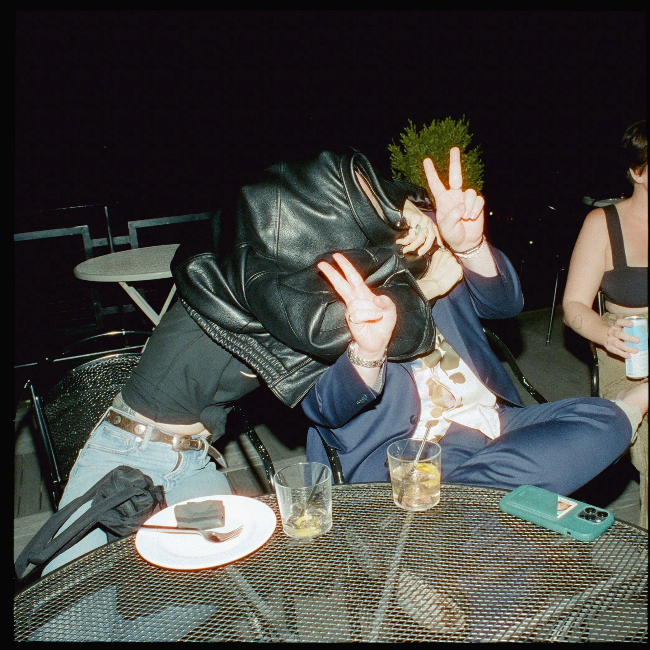 A couple cover their faces with a jacket and put up peace signs at a wedding afterparty