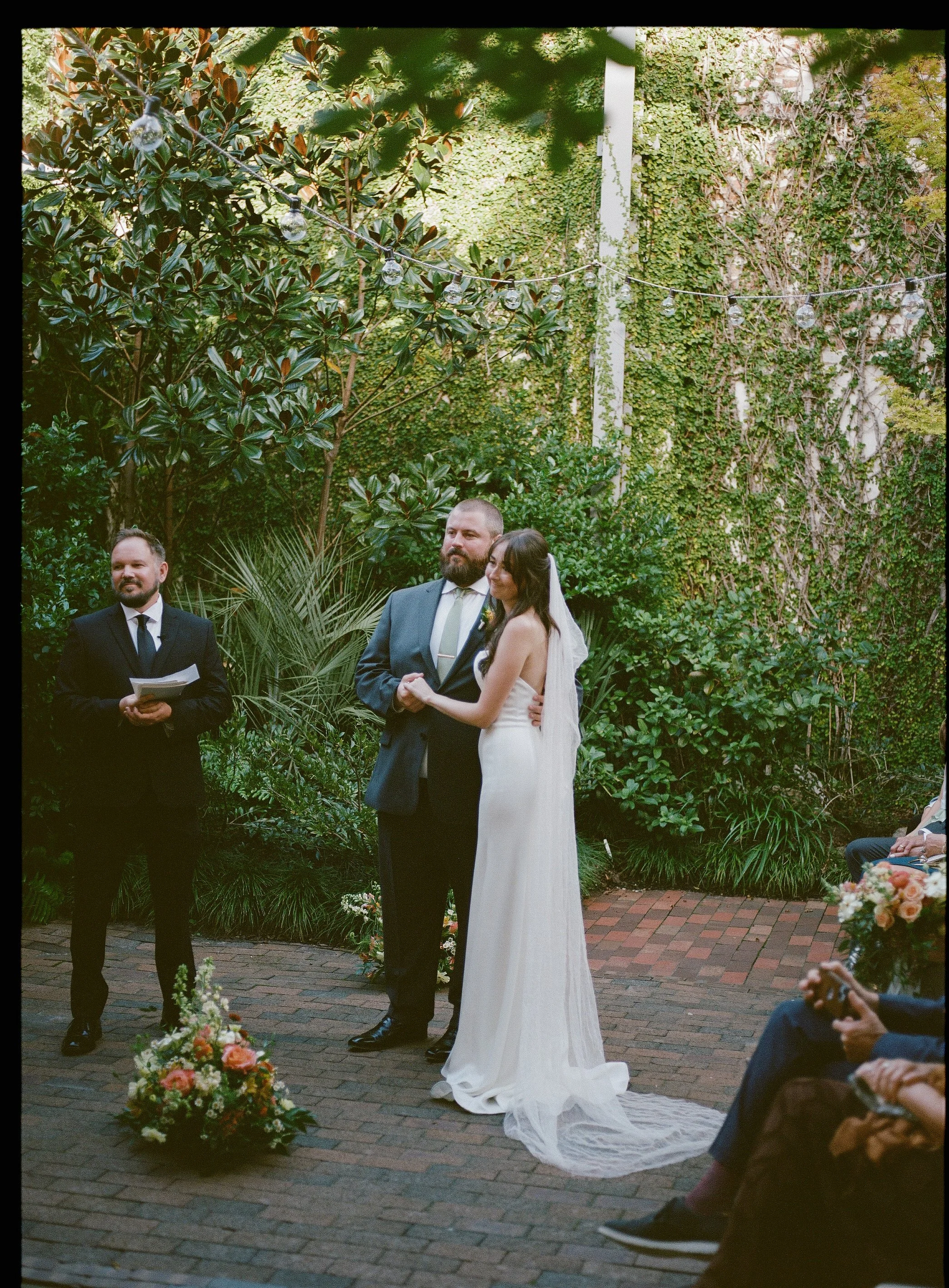 A bride and groom smile at a guest during their wedding ceremony