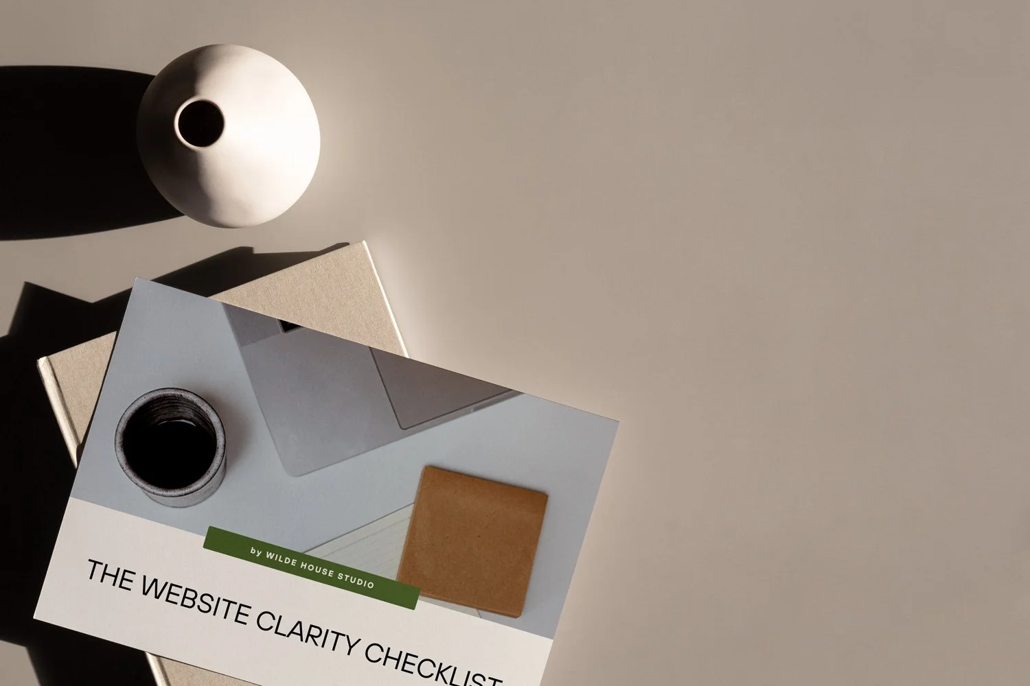 Overhead view of a white top with a white vase, a book, and a brochure titled 'The Website Clarity Checklist' by Wilde House Studio.