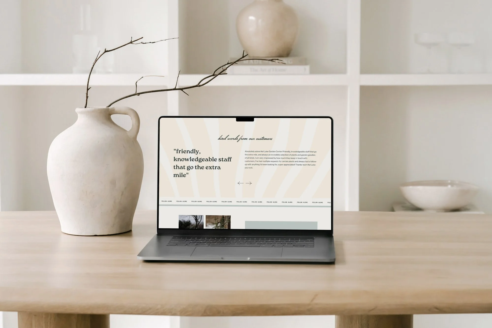 Laptop on a wooden table with a vase and a branch to the left, and a bowl to the right, in a neutral-toned room.