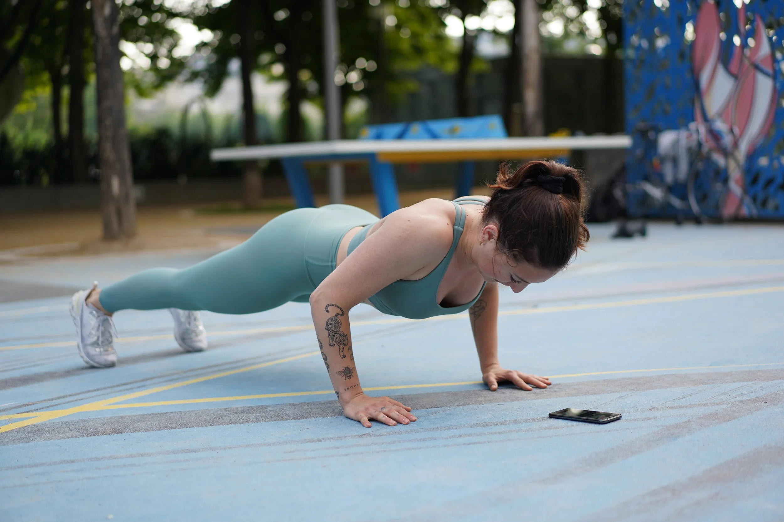 Une femme en tenue de sport effectuant une pompe sur un terrain de sport en extérieur.
