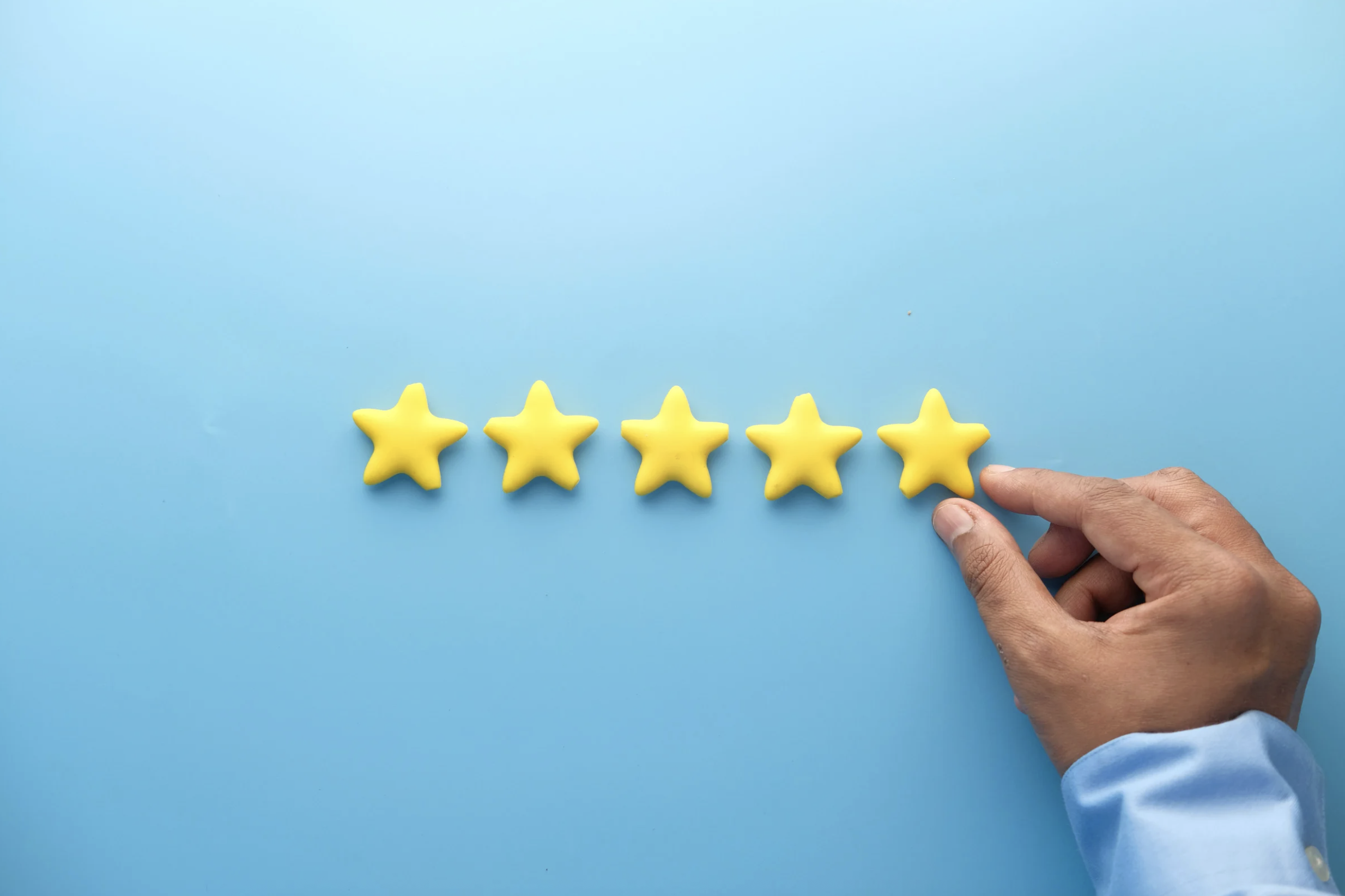 Cinq étoiles jaunes en forme d'étoile sur un fond bleu clair, avec une main droite ajustant la dernière étoile.