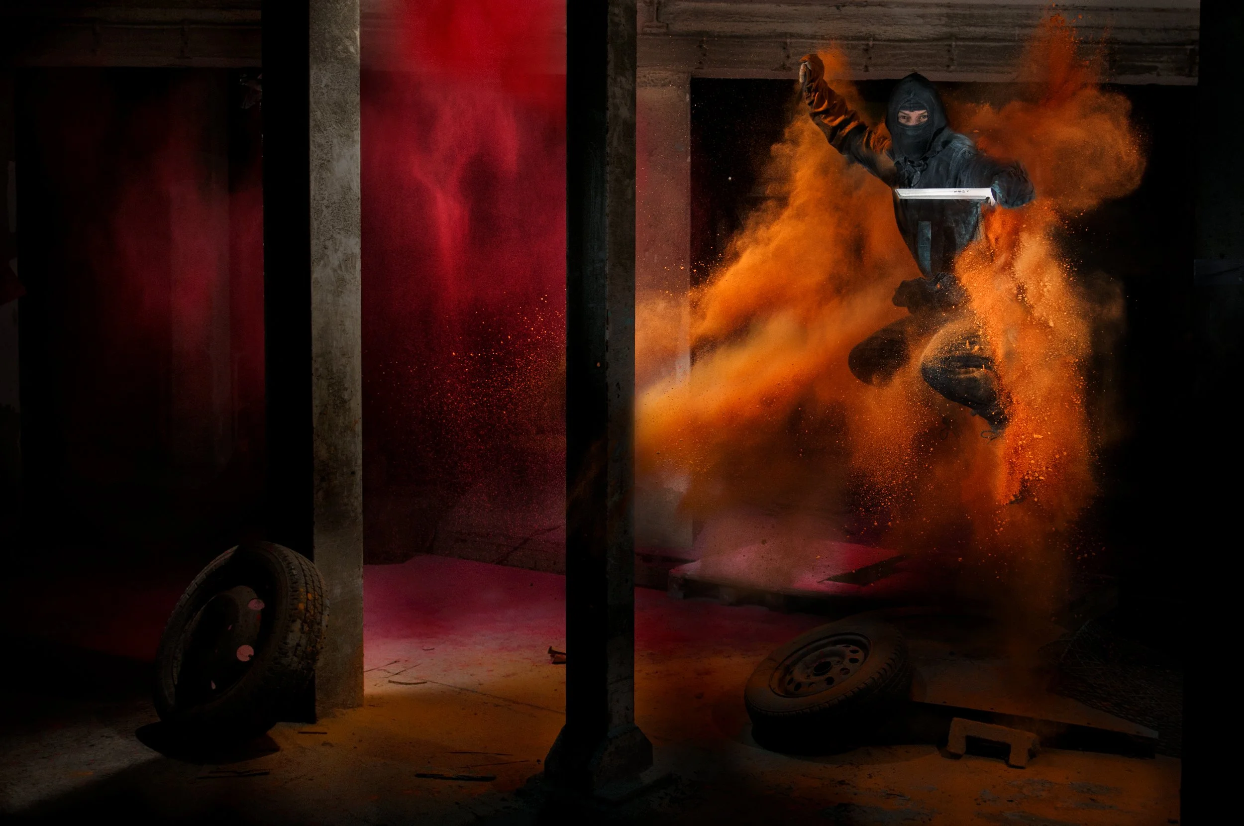 A ninja jumping mid air with swords raised surrounded by orange and red powder in a disused factory