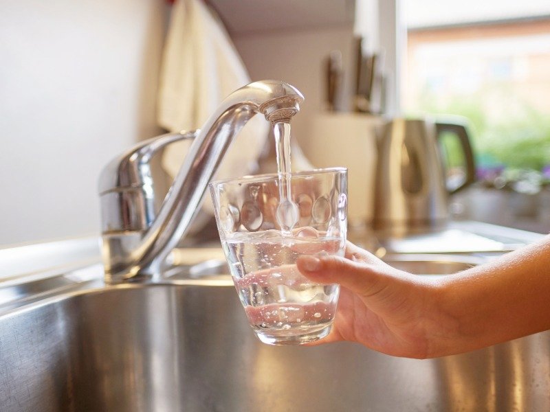 A glass of tap water being filled at a kitchen sink, representing well water testing for New Hampshire home buyers